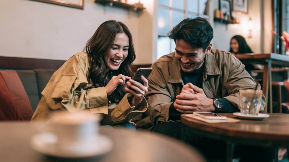 Two guests at a café table laughing as they order on a phone