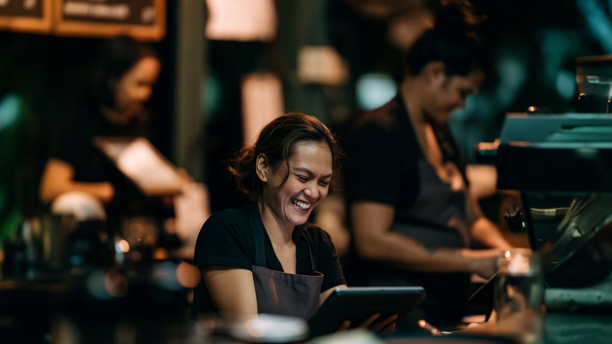 A café cashier smiling as she checks an order on a tablet at the counter